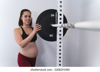 Pregnant Woman Placing Weights On A Barbell In A Squat Rack In A Home Gym