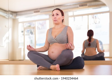 Pregnant woman practices yoga in the hall. Easy Pose or Sukhasana