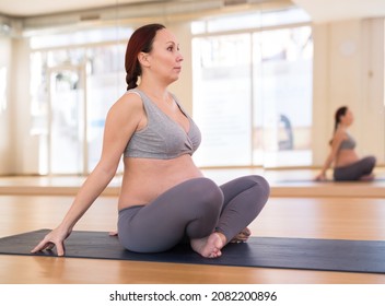 Pregnant woman practices yoga in the hall. Easy pose or Sukhasana