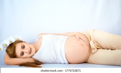 Pregnant woman practicing breathing prenatal exercises with beautiful flowers orchids on white background. Relaxation and delivery preparation mindfulness concepts. Sports concept.