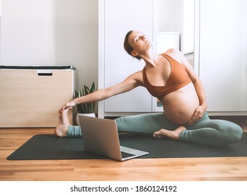 Pregnant Woman Practicing Yoga At Home With Laptop. Expectant Mother Doing Prenatal Video Training Class Indoors. Female Exercise, Meditate During Pregnancy. Online Fitness Class On Digital Devices.