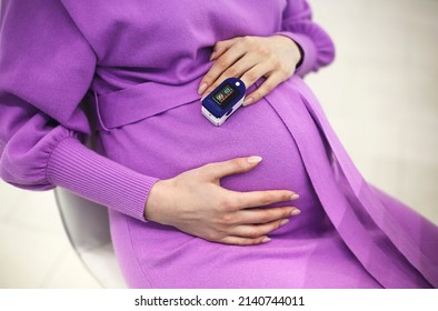 Pregnant woman with pulse oximeter on finger. Doctor measuring oxygen saturation level while visiting expectant mother with coronavirus disease at home, cropped. Pregnancy and covid-19 concept
