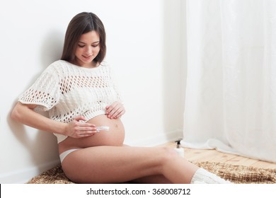 Pregnant woman putting cream on her belly to avoid stretch marks