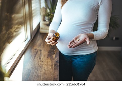 Pregnant Woman Reading Label On Bottle With Medicine, With Vitamins. Female At Home In Bed With Glass Of Water Medicine. Pregnancy, Health, Pharmaceuticals, Care And People.