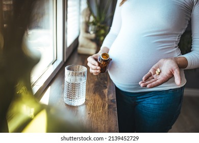 Pregnant Woman Reading Label On Bottle With Medicine, With Vitamins. Female At Home In Bed With Glass Of Water Medicine. Pregnancy, Health, Pharmaceuticals, Care And People.