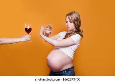 Pregnant woman refuses to drink wine, making stop gesture to glass on yellow background