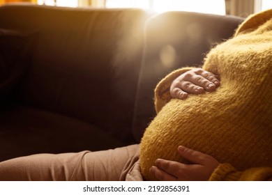 Pregnant woman relaxing at home in the sofa in the morning during sunrise with lens flare and sunlight. - Shutterstock ID 2192856391