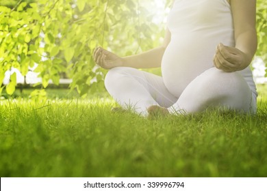 Pregnant woman relaxing in nature on a beautiful sunny day.A crop of a pregnant woman's stomach with field in the background.