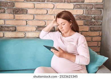 Pregnant woman relaxing on couch using tablet in comfortable home setting with brick wall background - Powered by Shutterstock