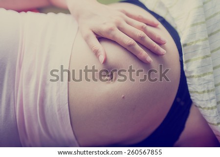 Pregnant woman relaxing on her back on a bed with her hand on her swollen bare belly as she bonds with her unborn baby, closeup view of her stomach and hand, toned retro effect.