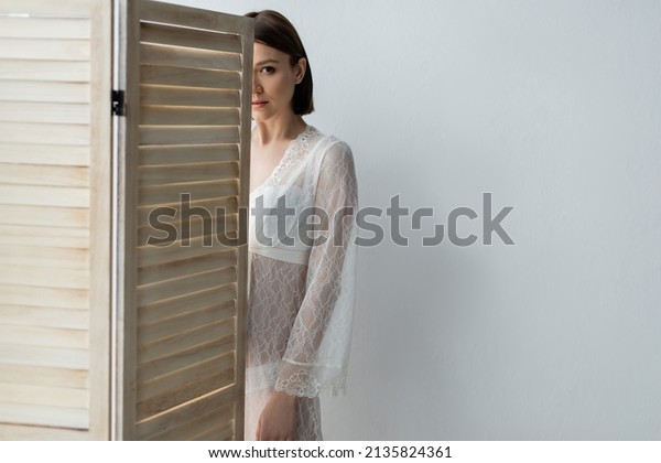 Pregnant woman in robe standing near folding screen\
at home