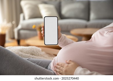 Pregnant Woman Showing Blank Smartphone Screen While Resting On Couch At Home. Expectant Mom Holding Mobile Phone With Copy Space For Pregnancy Track App, Touching Big Belly. Close Up