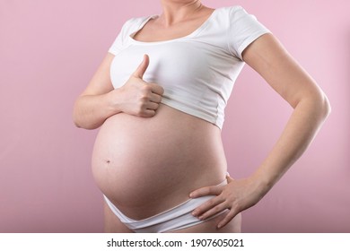 A pregnant woman shows a thumb up. Big pregnant belly.