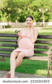 pregnant woman sits on a park bench and talking on phone. - Shutterstock ID 2310361853