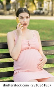 pregnant woman sits on a park bench and talking on phone. - Shutterstock ID 2310361857
