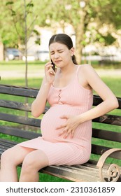 pregnant woman sits on a park bench and talking on phone. - Shutterstock ID 2310361859