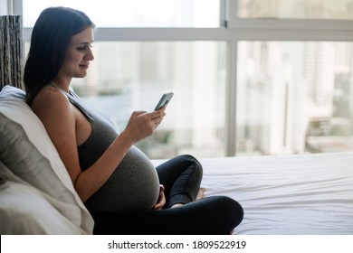 Pregnant woman sitting in bed relaxing looking at her phone third trimester 