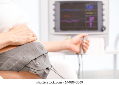 Pregnant woman sitting in clinic performing cardiotocography (CTG). Cardiotocograph machine aka Electronic Fetal Monitor (EFM) recording fetal heartbeat and uterine contractions during pregnancy