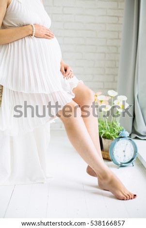 Pregnant woman sitting on a bed in a white dress