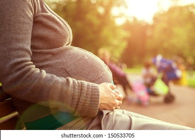 Pregnant woman sitting on a bench. on background the children play. warm weather