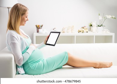 Pregnant woman sitting on couch and using tablet