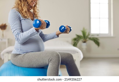Pregnant Woman Sitting On Fit Ball And Doing Physio Therapy Exercises With Light Weights. Active Lady Balancing On Fitball With Dumbbells In Hands, Cropped Shot. Pregnancy And Prenatal Workout Concept