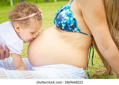 Pregnant woman sitting on the lawn, with baby kissing her belly. - Powered by Shutterstock