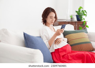 Pregnant woman sitting on sofa and using smartphone - Powered by Shutterstock