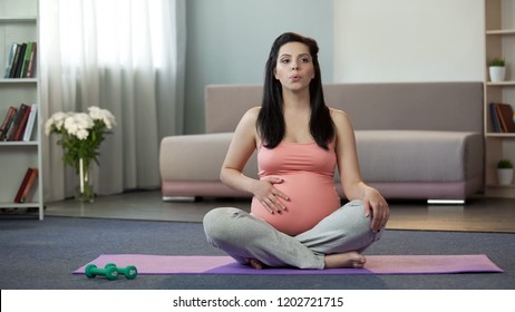 Pregnant Woman Sitting On Yoga Mat Doing Breathing Exercises And Massaging Belly