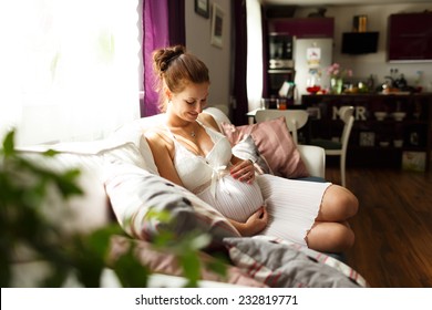 Pregnant woman sitting relax on bed. Sitting on sofa. Pregnant woman touching her belly with hands, relaxing at home on the couch, pregnant mother keeping her hands on belly while looking at it