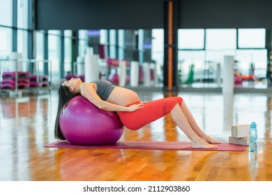Pregnant woman in sportswear doing fitness and stretching exercises with fitball at gym. Active expectant mother during prenatal pilates workout, selective focus. Pregnancy health and wellbeing