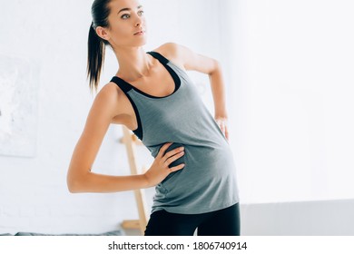 Pregnant Woman In Sportswear With Hands On Hips Training In Living Room