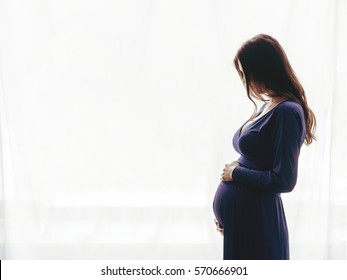Pregnant woman standing against the window - Shutterstock ID 570666901