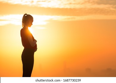  Pregnant woman standing in the beautiful sunset holding belly. Silhouette 