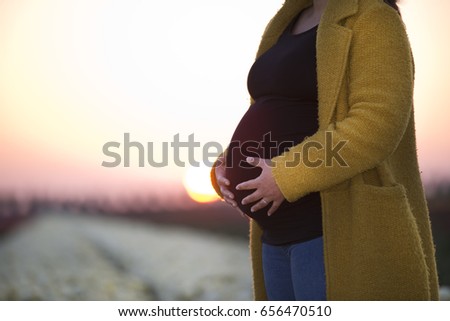 A pregnant woman standing in a field of flowers holding on to her tummy.