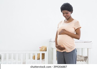 Pregnant woman standing near cradle and smiling while looking at her stomach