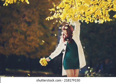 Pregnant woman standing in white coat outdoors. Pregnant woman holding a bouquet of yellow leaves. Pregnant woman walks in autumn park. Waiting for the baby. Walk outdoors in autumn day