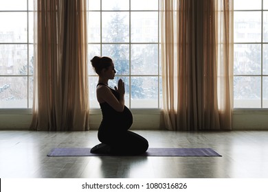 Pregnant Woman Standing In Yoga Pose In Front Of Big Windows. Practicing Healthy Lifestyle While Preparing To Become a Mother. Fitness For Future Moms. Sie View.