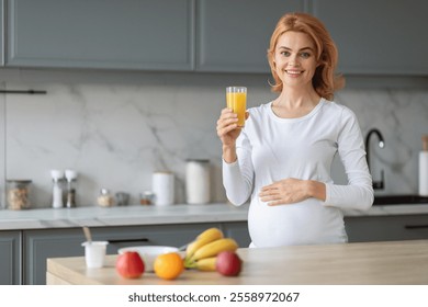 A pregnant woman stands in a stylish kitchen, joyfully holding a glass of orange juice. Fresh fruits are displayed on the counter, creating a healthy atmosphere in her home. - Powered by Shutterstock