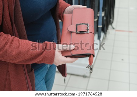 Pregnant woman in a store picks out a red clutch bag. The concept of fashion, buying new things and accessories. Hands close up shot