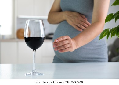 Pregnant woman stretch hand to glass of wine and want to have a drink. Pregnancy and bad habits. Prenatal care and alcohol abuse.
