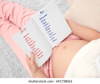 Pregnant Woman Studying List Of Names At Home. Concept Of Choosing Baby Name