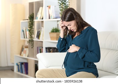 Pregnant woman suffering headache complaining sitting on a sofa in the living room at home - Shutterstock ID 1835926138