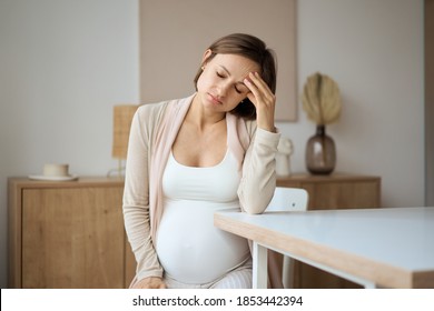 Schwangere, die an Kopfschmerzen leiden, während sie am Tisch sitzen. Hochwertiges Foto