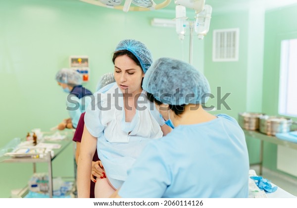 Pregnant\
woman in surgery room at birth. Friendly Staff preparation female\
patient for cesarean in operating room. Several doctors surrounding\
patient on operation table during\
cesarean.