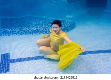 Pregnant Woman Swim, Dive In Swimming Pool. Aqua Fitness Healthcare Classes For Pregnancy. Underwater Picture Of Pregnant Woman Wearing Fashion Dress In Blue Deep Pool. Aquatic Therapy Workout.