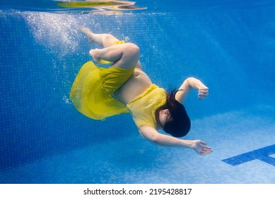 Pregnant Woman Swim, Dive In Swimming Pool. Aqua Fitness Healthcare Classes For Pregnancy. Underwater Picture Of Pregnant Woman Wearing Fashion Dress In Blue Deep Pool. Aquatic Therapy Workout.