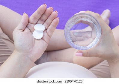 Pregnant Woman Takes Food Supplement Vitamins Calcium Vitamin C Or Aspirin.hand With Glass Full Filed With Water And Capsule In Another,white Round Pills Tablets.fenale In Last Trimester Of Pregnancy,