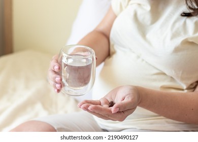 Pregnant Woman Takes Food Supplement Vitamins Calcium Vitamin C Or Aspirin.hand With Glass Full Filed With Water And Capsule In Another,white Round Pills Tablets.fenale In Last Trimester Of Pregnancy,