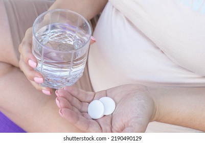 Pregnant Woman Takes Food Supplement Vitamins Calcium Vitamin C Or Aspirin.hand With Glass Full Filed With Water And Capsule In Another,white Round Pills Tablets.fenale In Last Trimester Of Pregnancy,